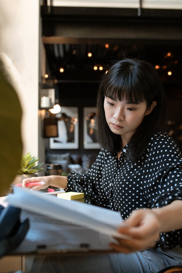 Asian woman reviewing documents at a modern office desk, focused and professional.